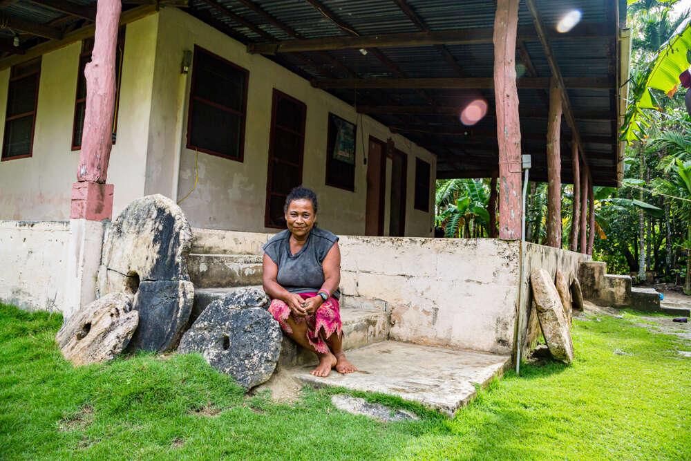 Yap island, Micronesia - Local Micronesian woman sitting on the porch alongside three rai stones. Photo: maloff/Shutterstock.com