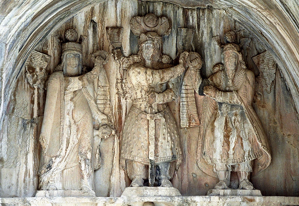 Taq-e Bostan high-relief of the investiture of Khosrow II (r. 590 to 628). The king (center) receives the ring of kingship from Mithra (right). On the left, apparently sanctifying the investiture, stands a female figure generally assumed to be Anahita.