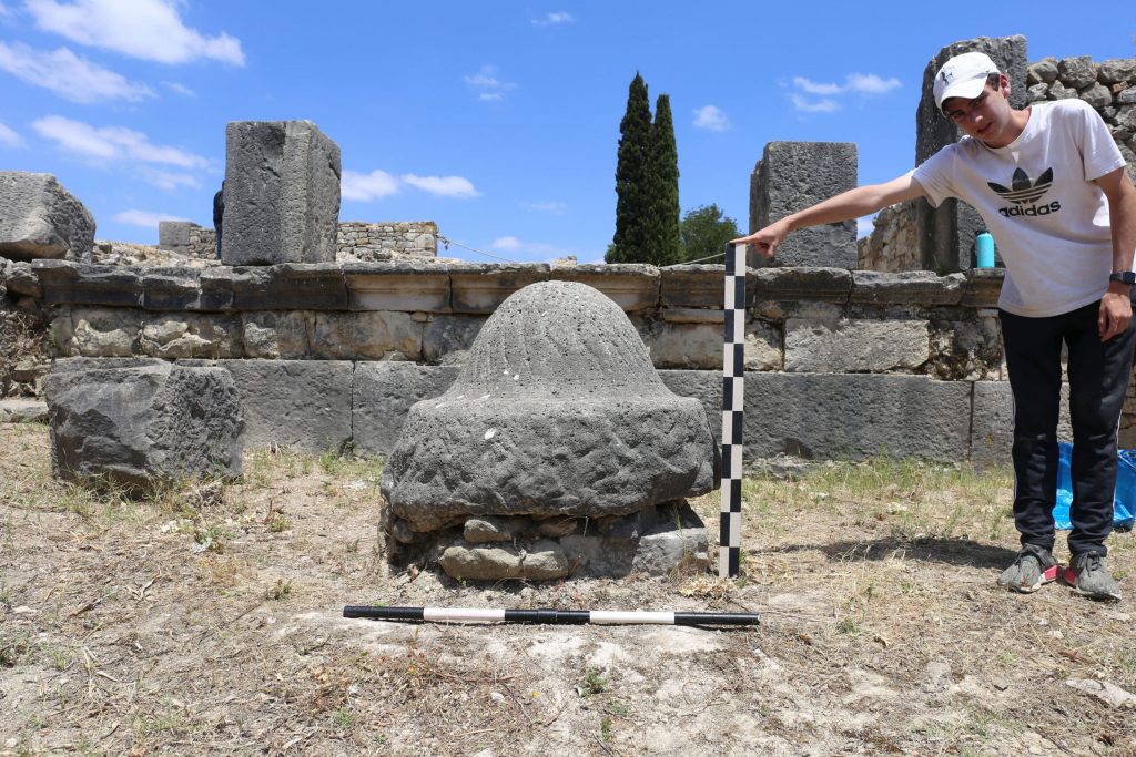 An olive millstone in Volubilis. Research assistant Drew Messing holds a tool for scale. Photo: Jared Benton.