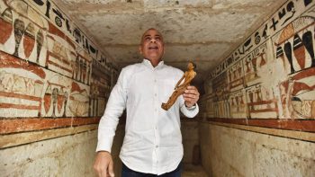 Mostafa Waziri, Secretary General of the Supreme Council of Antiquities, displays a small statue at a tomb decorated with hieroglyphics.