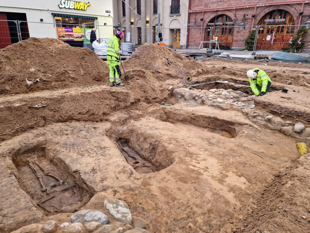 Archaeologists from the Cultural Environment of Halland and partners Lödöse Museum and Bohusläns Museum are working in the shaft. The southern foundation wall of the church can be seen behind the graves. Photo: Cultural Environment of Halland