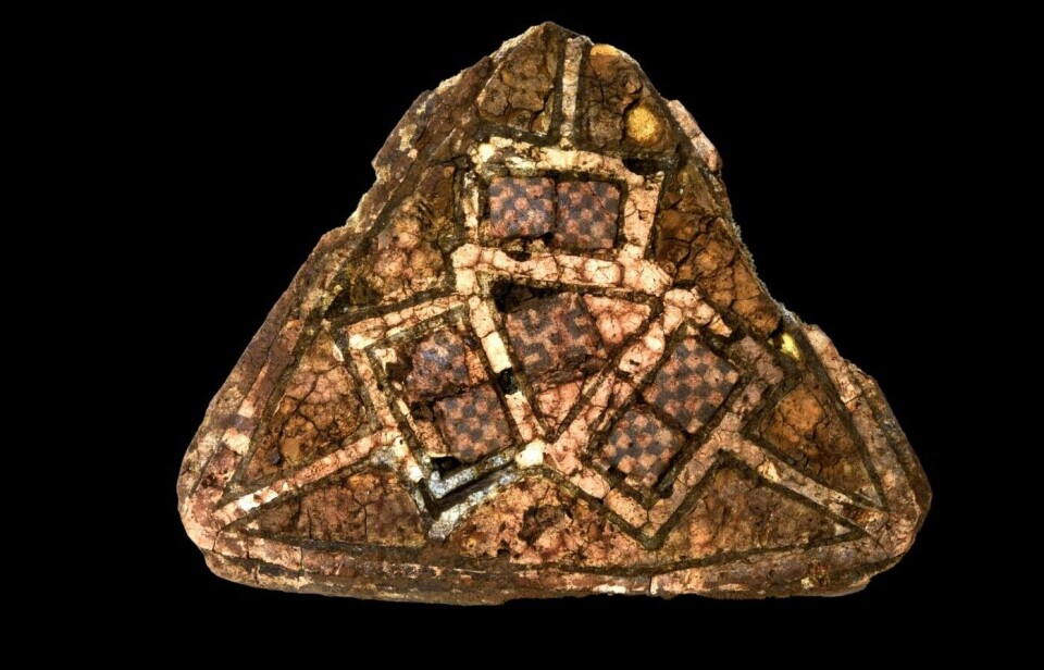 A triangular brooch featuring glass mosaic and gold enamel, likely from Ireland or England, was discovered in a grave within a rock crevice. The grave had previously been opened, with remnants of the grave goods found scattered outside and around it. Credit: University Museum of Bergen