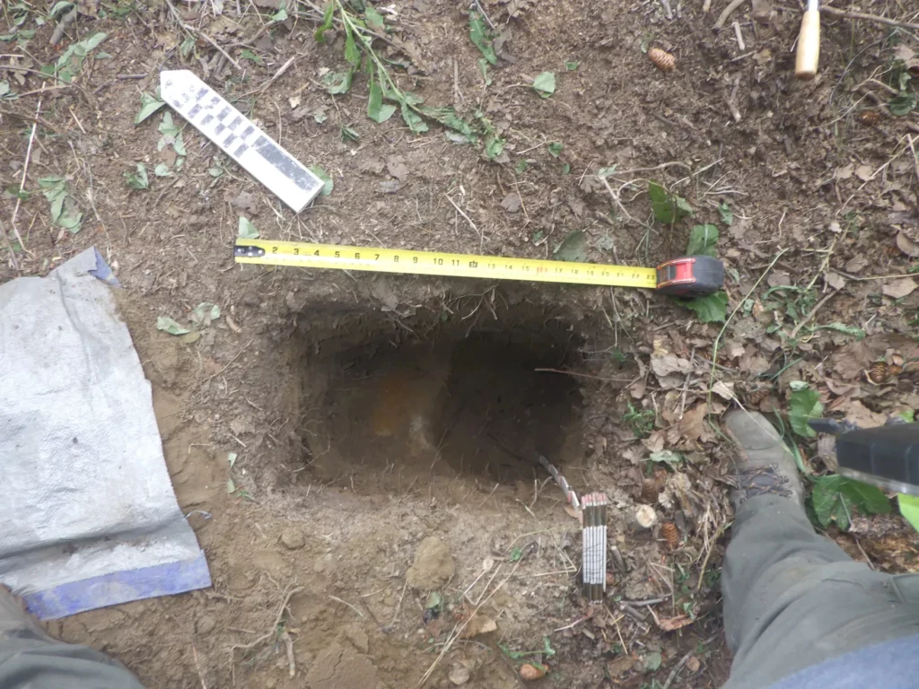 Researchers measure a test excavation they made into the wall of the cache during their visit in the summer of 2024. The white spot in the middle is the preserved birch bark. Credit: U.S. Air Force