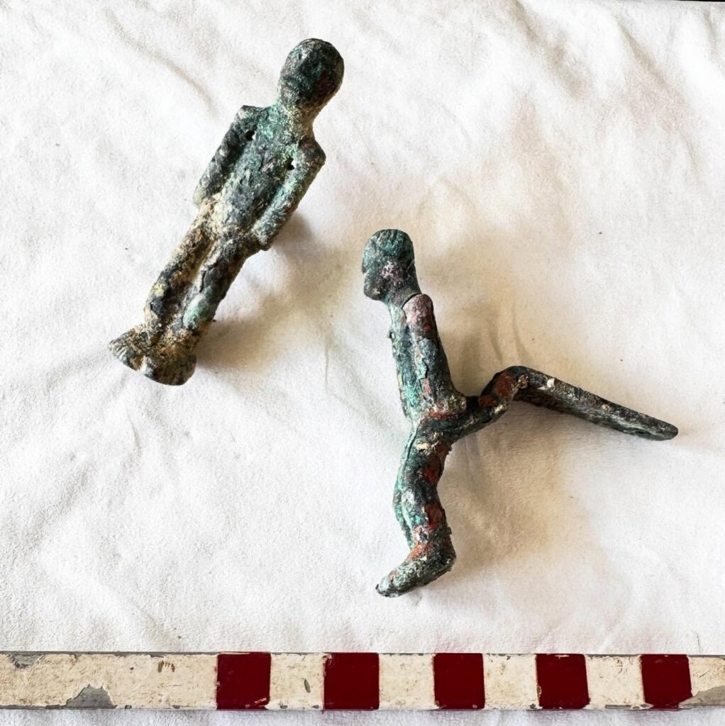 The three miniature bronze figures differ in form and detail, with one representing a small human figure, while another was found in a fragmentary state