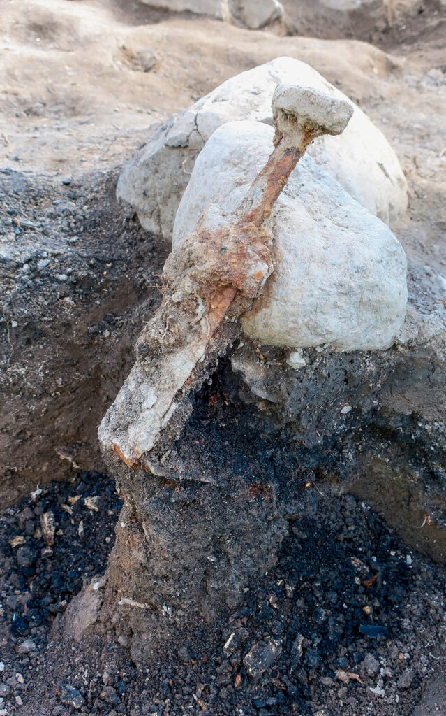The broken blade shows that the swords were forced into the ground with great strength. Around the blade lies the black cremation layer containing burned bones. Credit: Arkeologerna