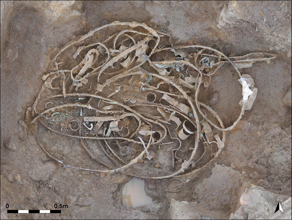 The bent iron tyres, hub elements and U-shaped iron brackets in Hoard 1 during excavation (photograph: Durham University). Credit: Adams S, 2026, Antiquity