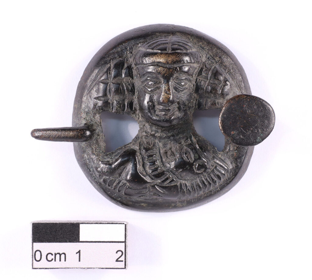  Circular belt buckle showing the bust of a woman cradling a baby. Parthian. Leaded bronze. (BM:2001,0404.1). © The Trustees of the British Museum.  Credit: Davis et al., 2026