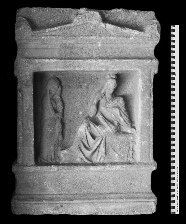  Carved from fine-grained white marble, it measures 76 centimeters high and takes the form of a schematic naiskos, a small temple-like architectural frame commonly used in Hellenistic funerary monuments. Çekilmez, M., et. al., 2026, OLBA