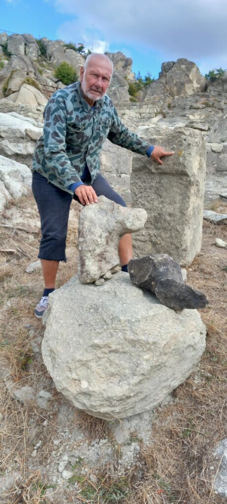 Prof. Nikolay Ovcharov beside a statue pedestal, male torso and animal sculpture fragment discovered at Perperikon.