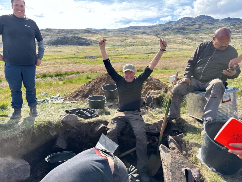 Archaeologists celebrating at an excavation site in Greenland, with Christian Edelfelt Koch Madsen raising his arms after the discovery of a medieval Norse grave.