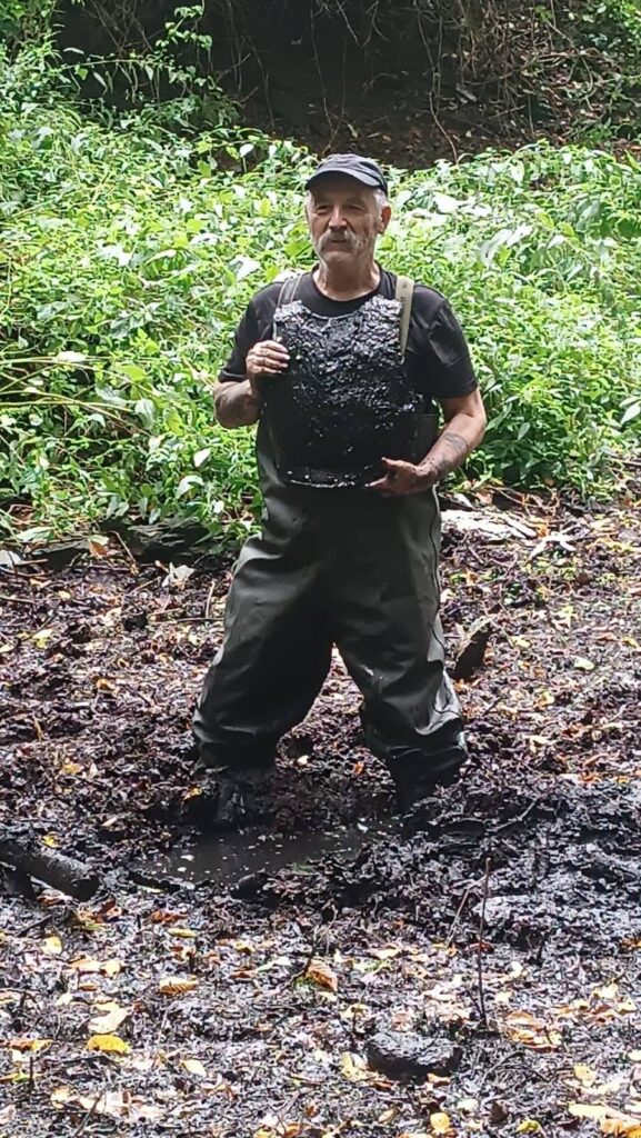 Wiesław Andrysiak holds the mud-covered 19th-century guard cuirass after searching the Pielaszkowice Palace moat, where the mud reportedly reached up to his waist. Credit: Muzeum Domu Śląskiego w Ziębicach