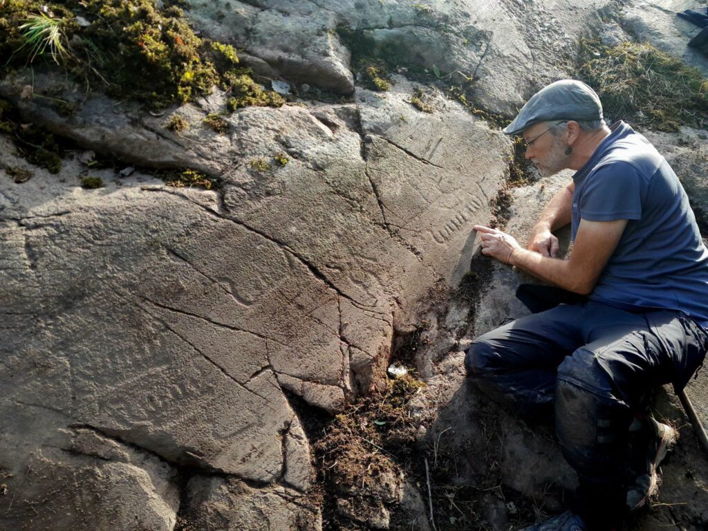 Researcher studying rock carvings on a granite panel at Trättelanda in Sweden’s Tanum World Heritage Site.
