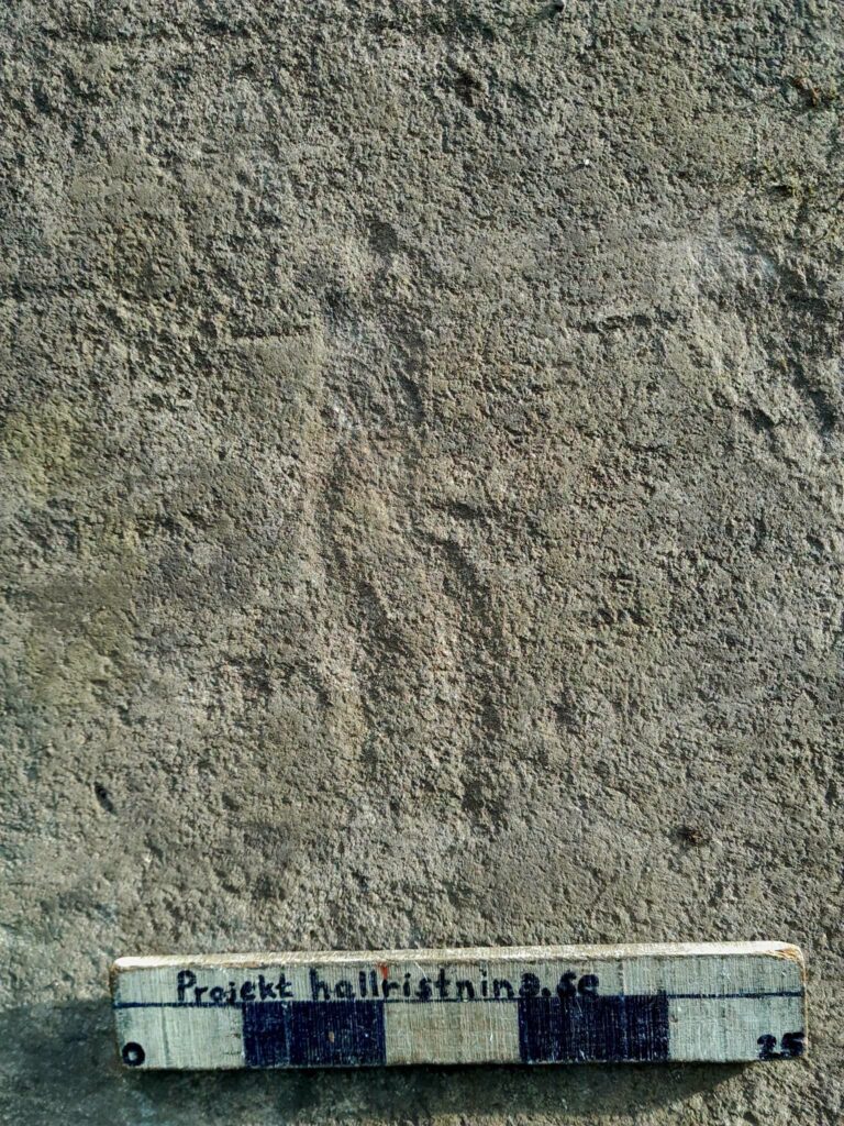 Close-up of a faint human figure carved into a rock surface, shown with a measuring scale.