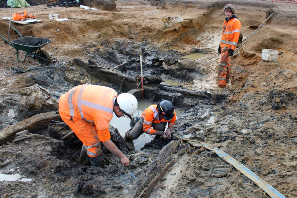 Archaeologists excavating preserved Bronze Age wooden remains in a waterlogged pit near Gloucester, England.