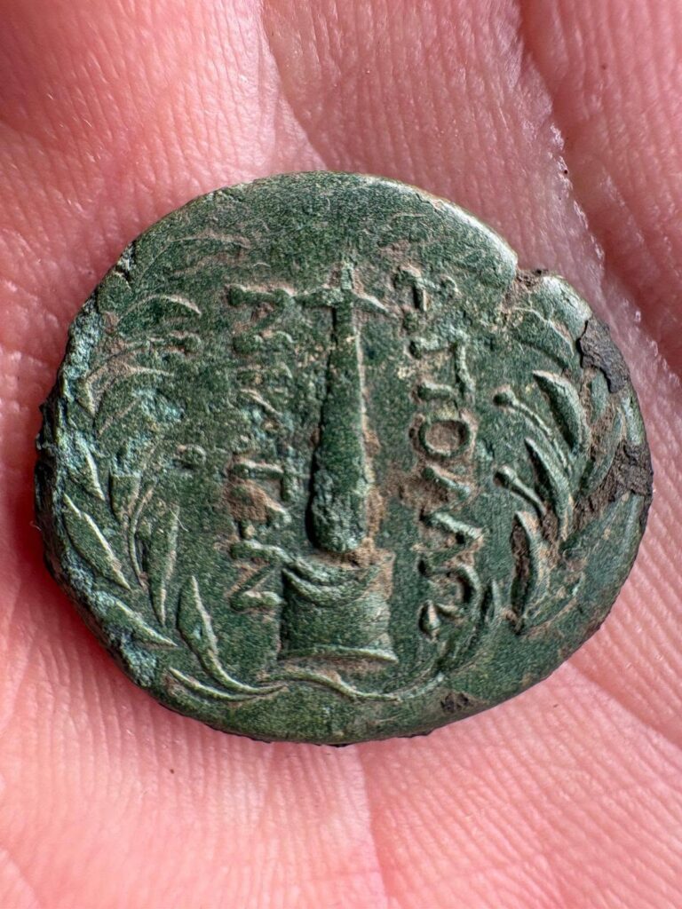 Close-up of an ancient Apollonian bronze coin with green patina, Greek inscriptions, an obelisk-like central motif, and a surrounding wreath.