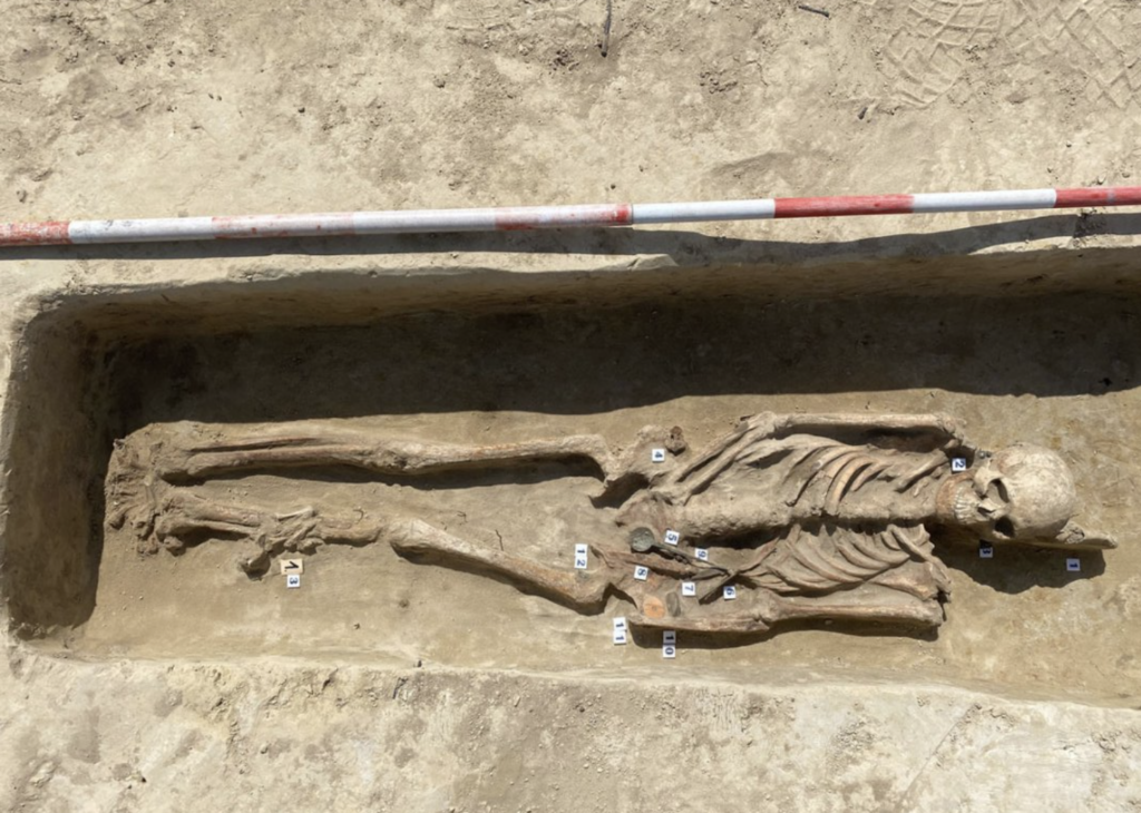 Archaeological excavation of a 1,400-year-old Avar woman's grave in Hungary, showing skeletal remains and personal objects found alongside her.