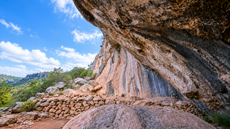 Wide view of the Badanj rock shelter near Stolac in Bosnia and Herzegovina, showing the large rock overhang and the surrounding valley landscape.