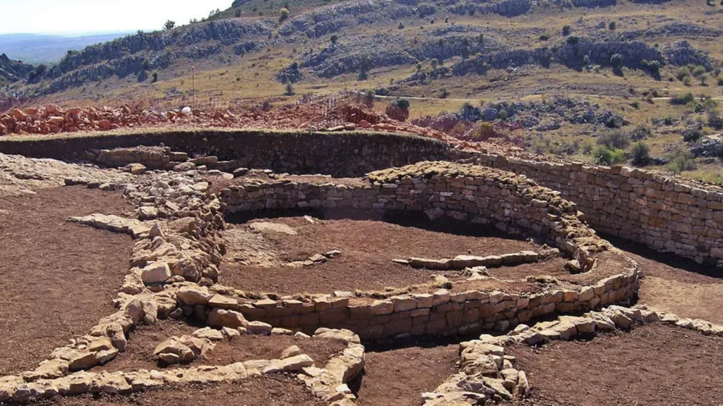 Excavated remains of a D-shaped Iron Age temple with curved stone walls at La Peña del Castro archaeological site in northern Spain.
