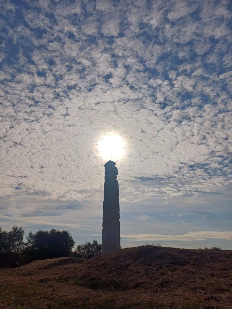 Tall ancient Doric column standing against a cloud-filled sky at the Shtyllas temple site in Albania.