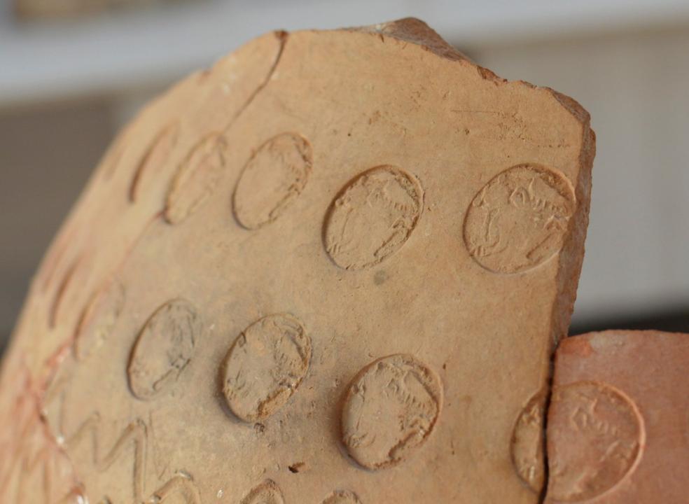 Close-up of an ancient ceramic fragment decorated with rows of circular impressions and incised patterns.
