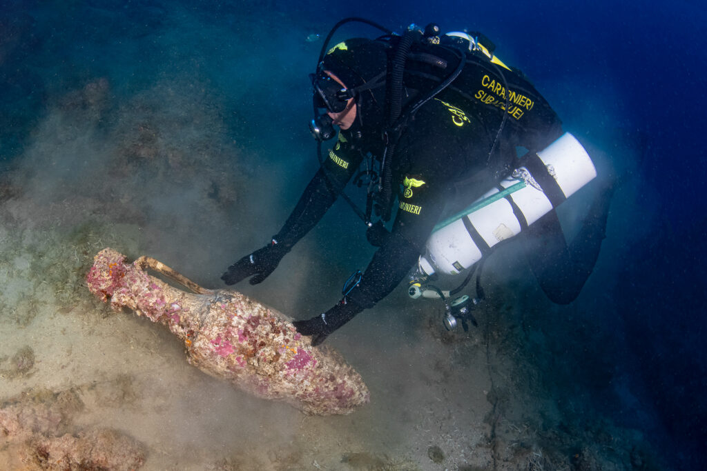 Underwater archaeologist inspecting an encrusted Roman wine amphora on the rocky seabed off Liguria.