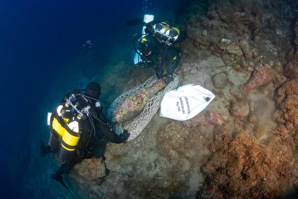 
Two Carabinieri divers securing an ancient Roman amphora in a recovery net underwater.