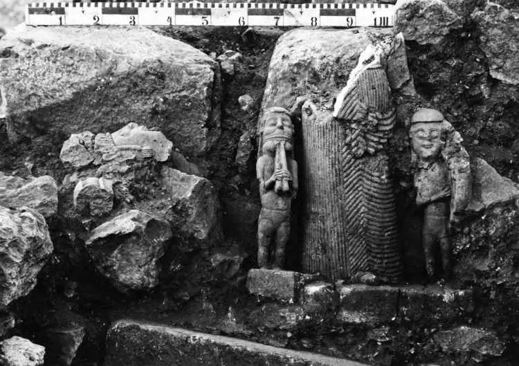 Black-and-white archival photograph of Hittite stone sculptures and carved fragments arranged in an excavation trench at Hattusa, with a measuring scale above them.