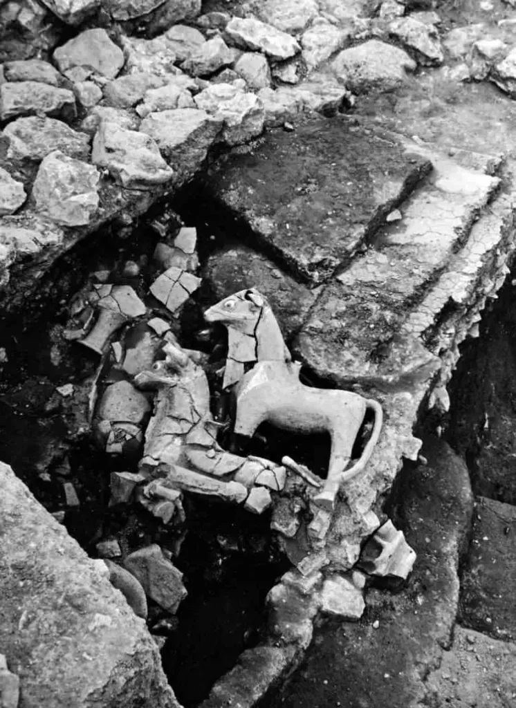 Black-and-white archival photograph of an archaeological excavation at Hattusa, showing animal-shaped artifacts, including a prominent bull figurine, surrounded by stones and fragments.