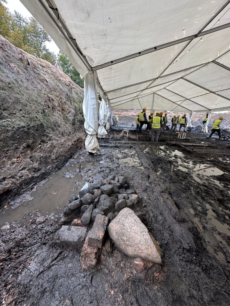 Archaeologists excavating waterlogged historical layers beneath a protective tent at the Siuru archaeological site in Tartu, Estonia.