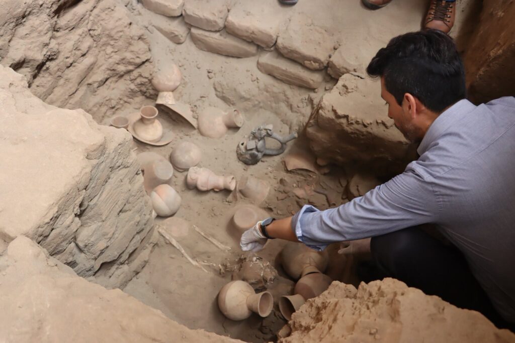 Archaeologist examining a Moche burial chamber filled with pottery vessels and human remains during excavations in Peru.