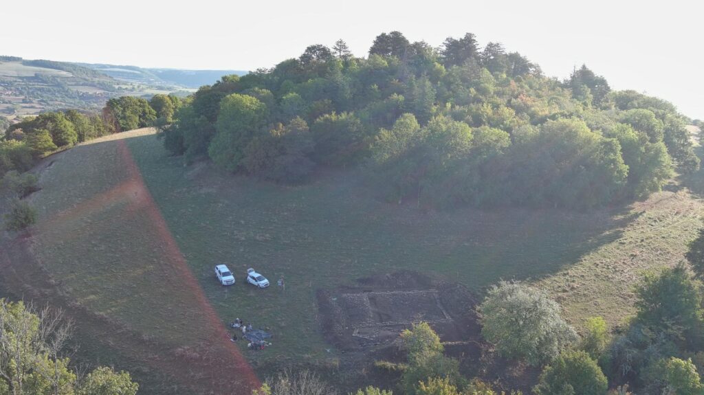 Drone view of the wooded Montagne de Saint-Laurent hilltop, with an archaeological excavation area and surrounding fields in Mesmont, France.