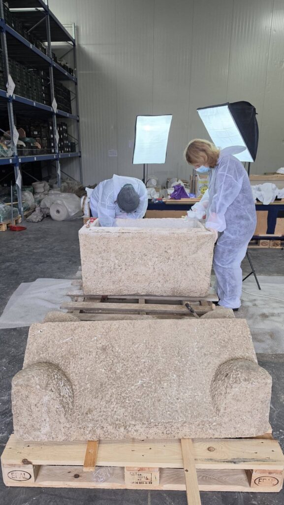 Archaeologists examining an open Roman stone sarcophagus in a conservation workspace