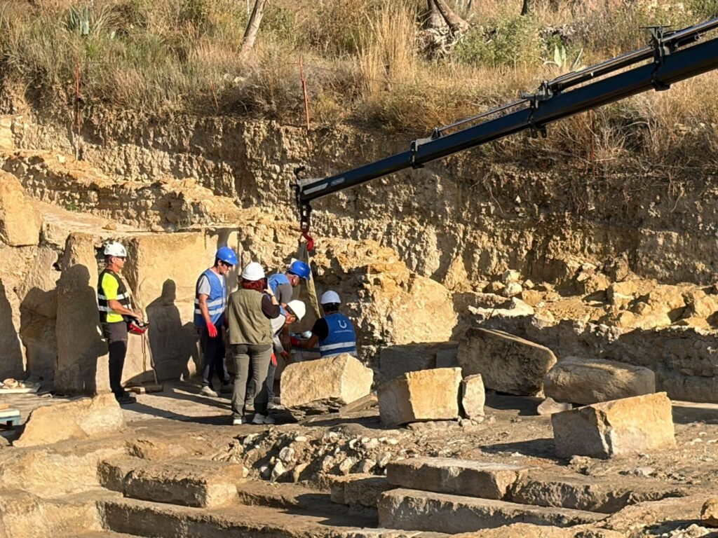 Archaeological team using lifting equipment to remove a Roman stone block from the Fortuna baths excavation in Murcia.
