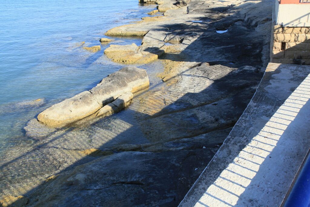 Ancient parallel cart ruts running across a limestone surface near St. George’s Bay in Birżebbuġa, Malta.
