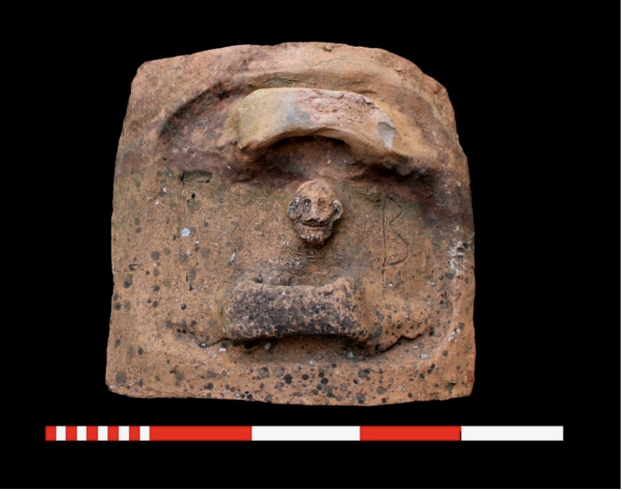  Wider view of a Roman-era terracotta sarcophagus lid from Attouda, showing the small Silenus-head relief and surrounding surface.