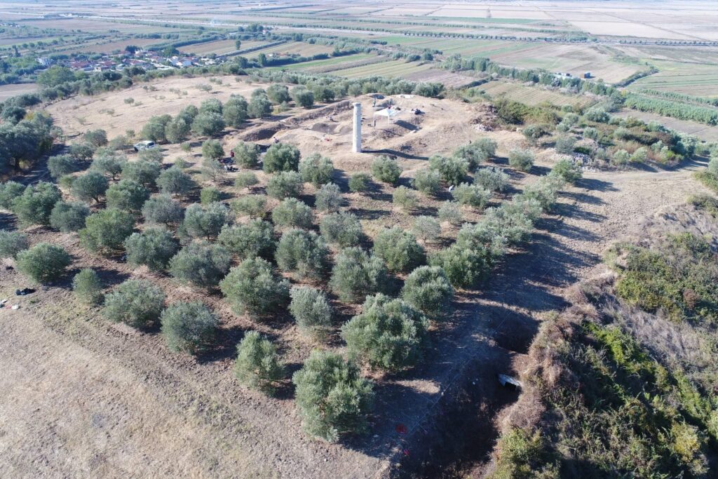 
 Wide aerial photograph of the Shtyllas temple site in Albania, showing a solitary Doric column, olive groves, and the surrounding countryside.