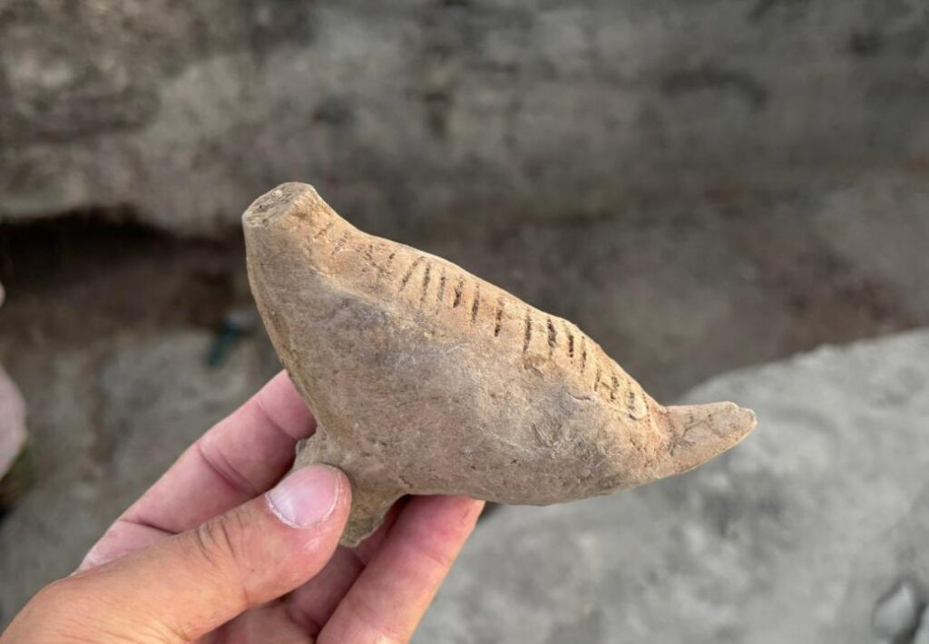 Ancient ceramic bird figurine with incised decorative lines, held in a person's hand.