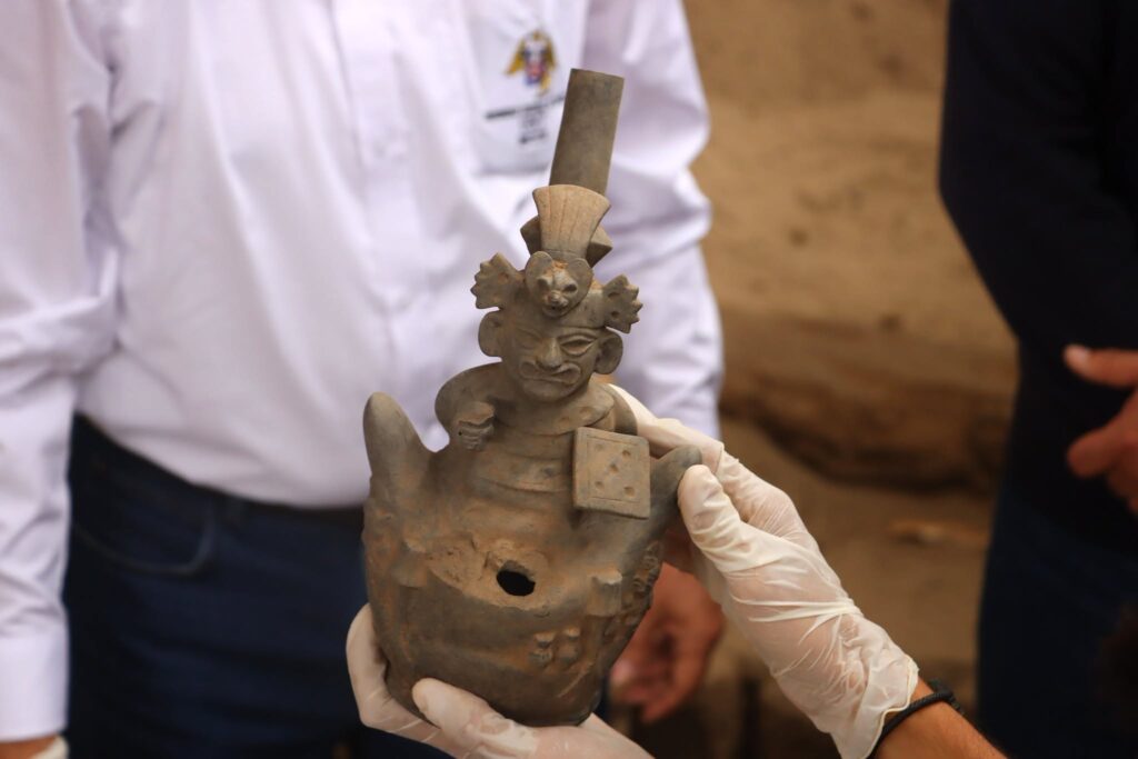 Moche ceramic vessel featuring a supernatural figure with bird-like characteristics, displayed by a researcher wearing protective gloves.