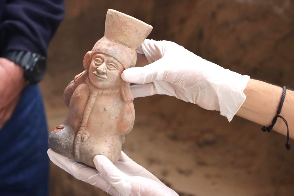 Ancient Moche ceramic vessel depicting a prisoner with a rope around his neck, held by a researcher wearing gloves.