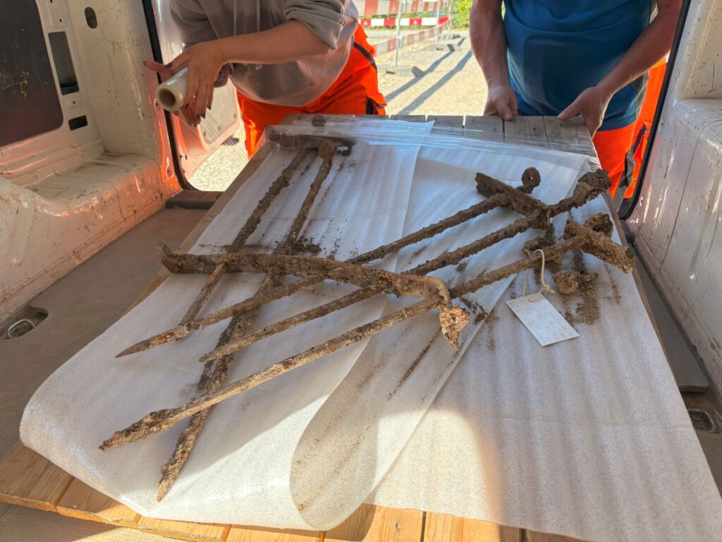 Excavated Roman iron window grille resting on protective material during transportation, showing its corroded metal bars and surviving fastening elements.