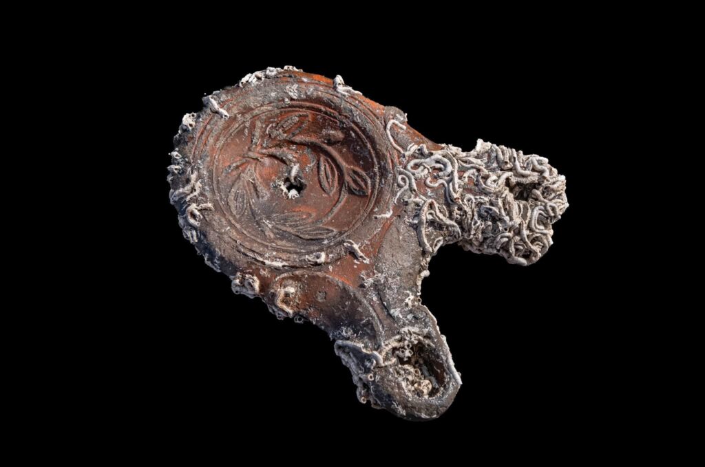 Ancient ceramic oil lamp decorated with a floral motif and covered with marine encrustations, recovered from Alexandria’s Eastern Harbour.